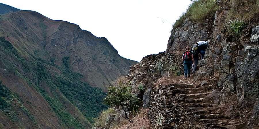 Hikers climbing the original Inca stone steps above a green mountain valley