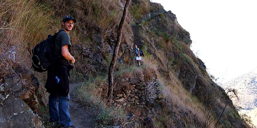 Smiling hiker with a backpack on the original Inca trail, with stone steps climbing the steep slope behind
